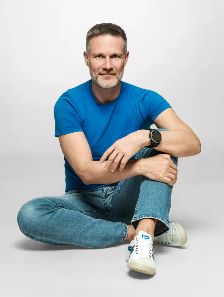 Piotr Urbanik – coach przywódców i liderów biznesu, siedzący w niebieskiej koszulce na szarym tle
