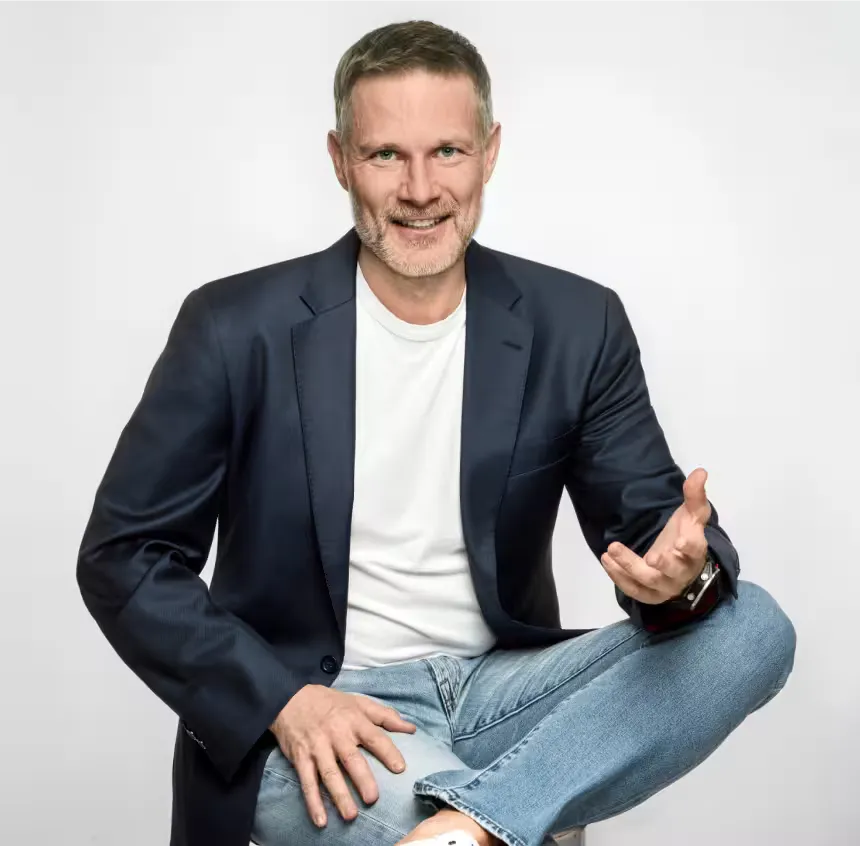 Piotr Urbanik – coach liderów biznesu podczas rozmowy, gestykulujący w granatowej marynarce na jasnym tle