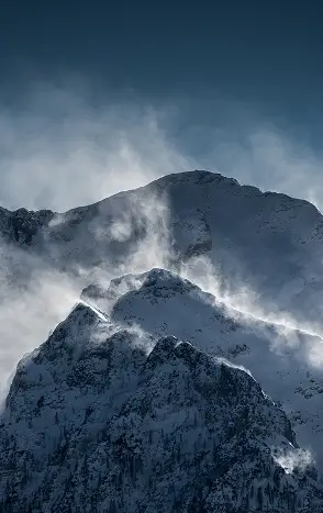 zdjęcie przedstawiające wysokie skaliste góry ze śniegiem na szczycie i lekką mgłą